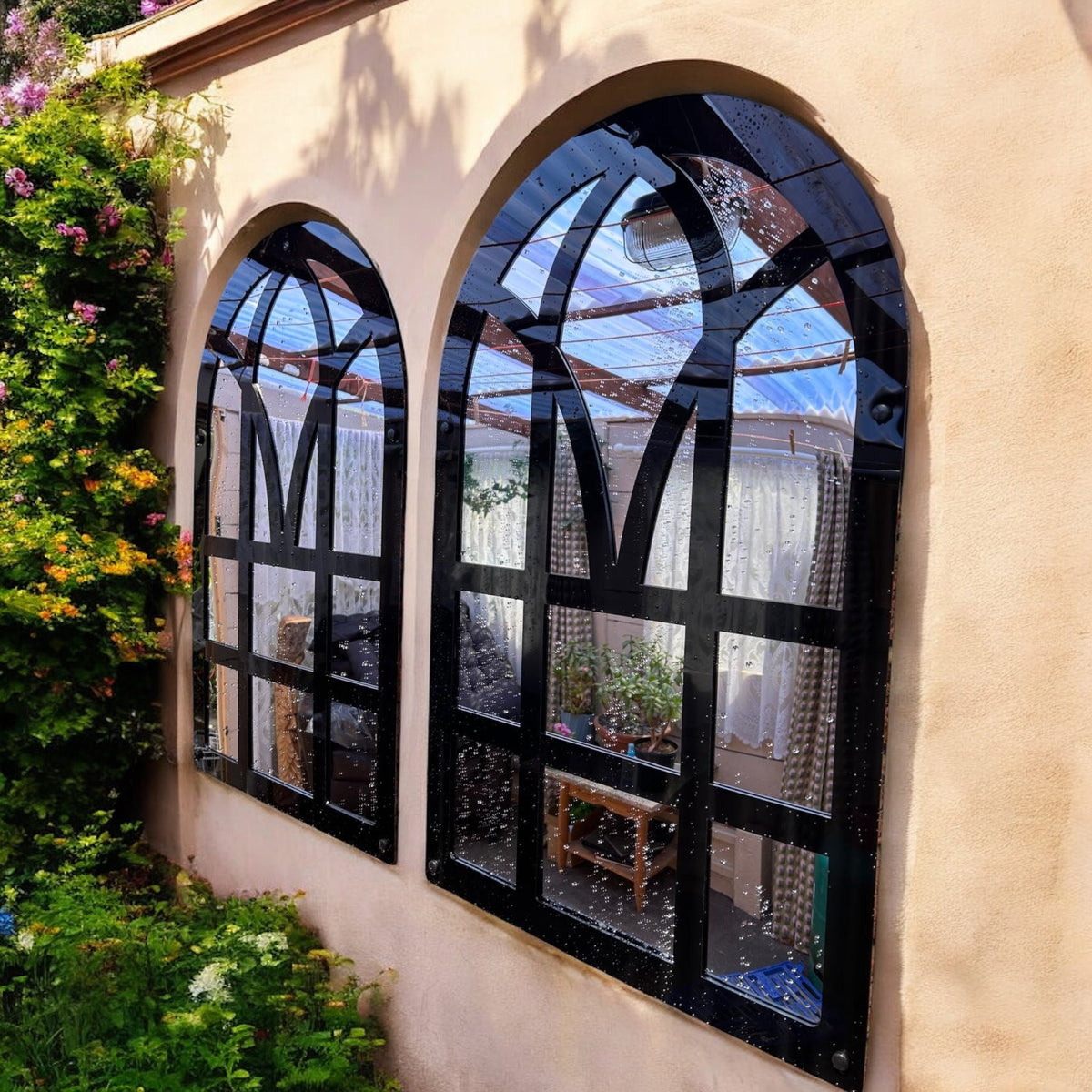A pair of black-framed Victorian arch garden mirrors mounted on a tan stucco exterior wall.