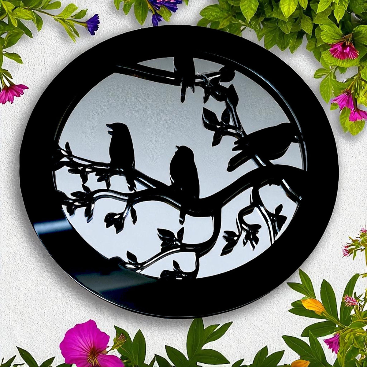 Round black garden mirror featuring a silhouette design of birds perched on leafy branches.