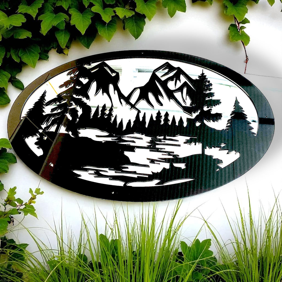 Oval black metal garden mirror featuring a laser-cut mountain range and pine forest silhouette.