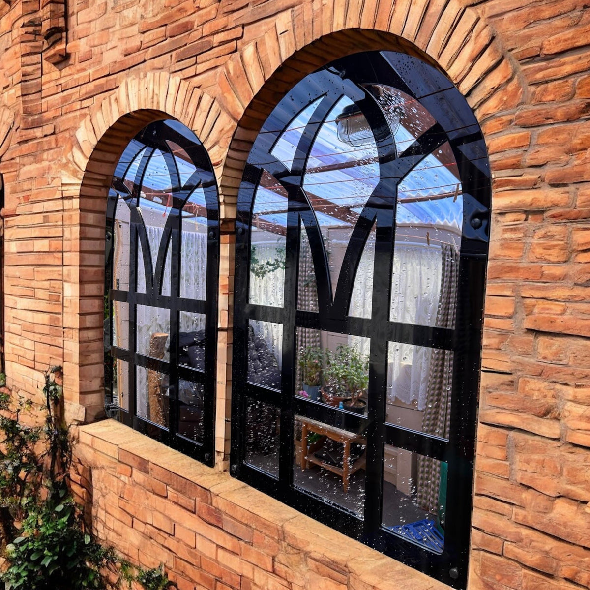 Pair of black-framed Victorian arch garden mirrors mounted on a red brick wall.