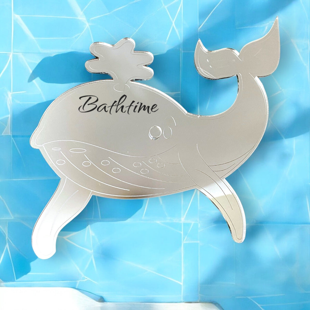 Etched whale-shaped mirror with "Bathtime" text and water spout, on a blue background.