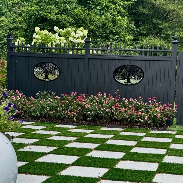 Two oval black Tree of Life garden mirrors mounted on a dark vertical slat fence.