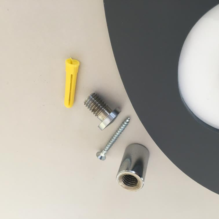 Hardware installation kit showing yellow wall plug, silver screws, and chrome standoffs next to a mirror.