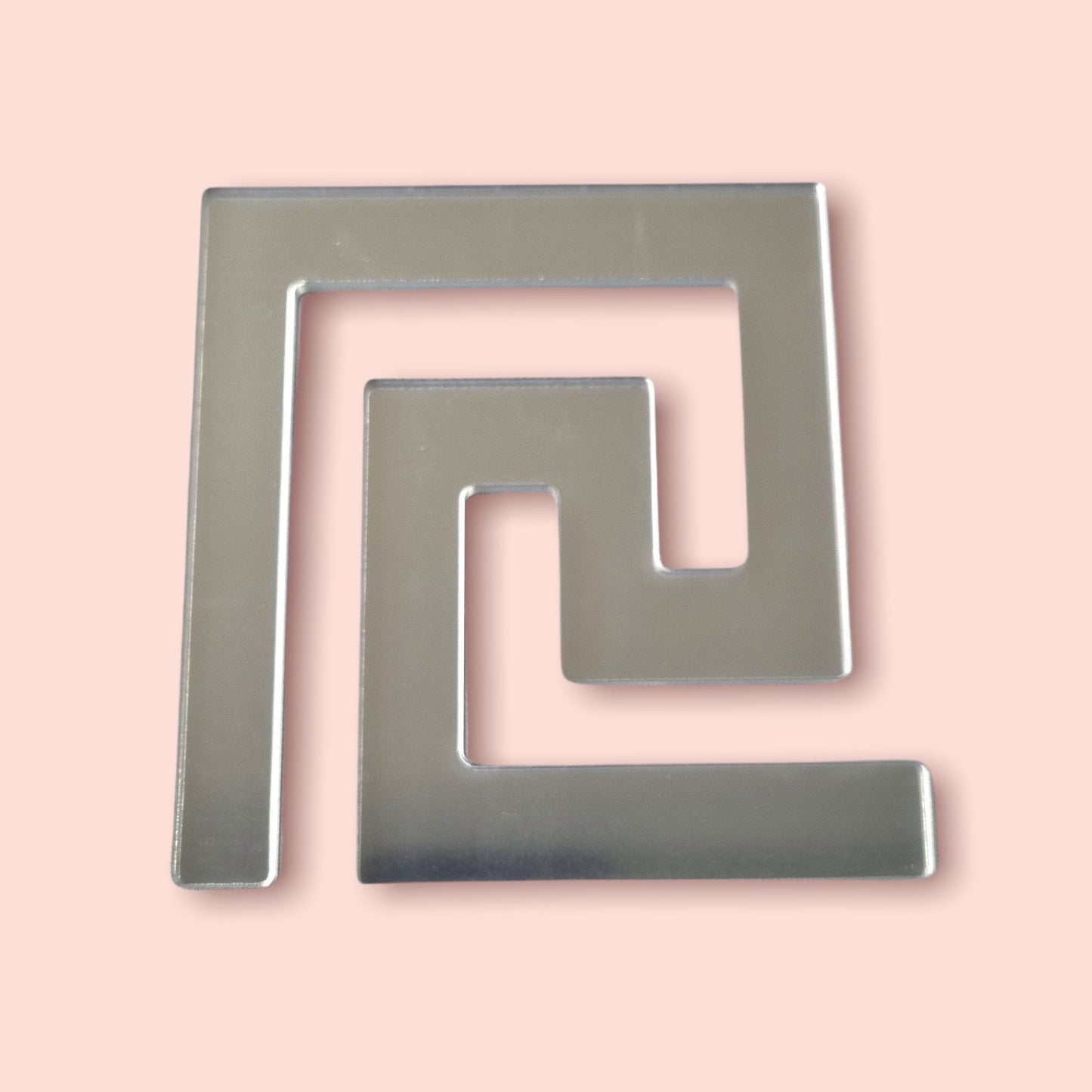 Silver mirror acrylic Greek key tile in a continuous geometric meander pattern on a peach background.