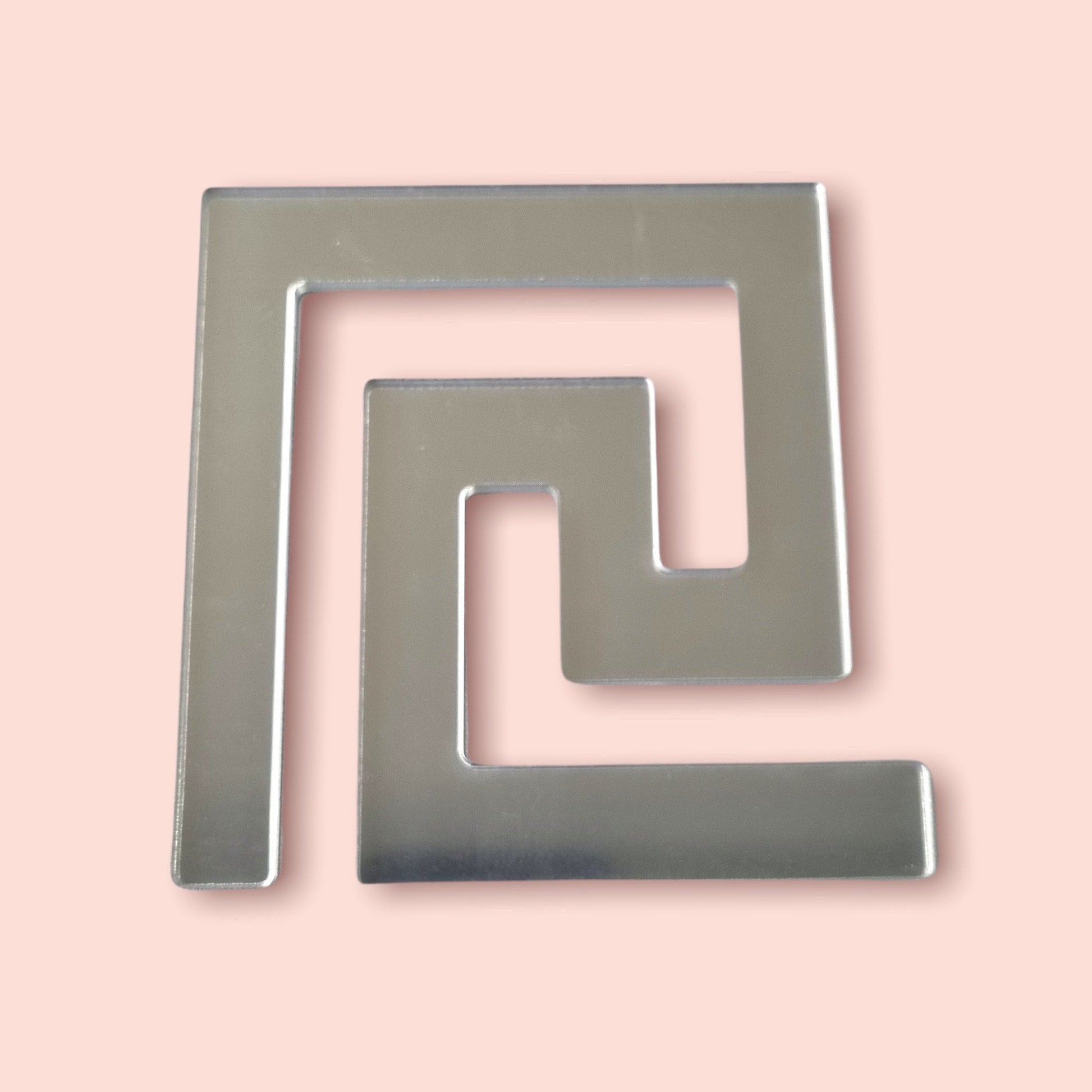 Silver mirror acrylic Greek key tile in a continuous geometric meander pattern on a peach background.