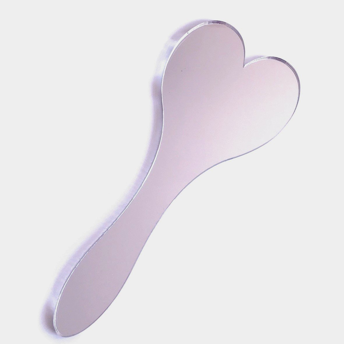 Silver heart-shaped hand-held mirror with an attached handle on a plain background.