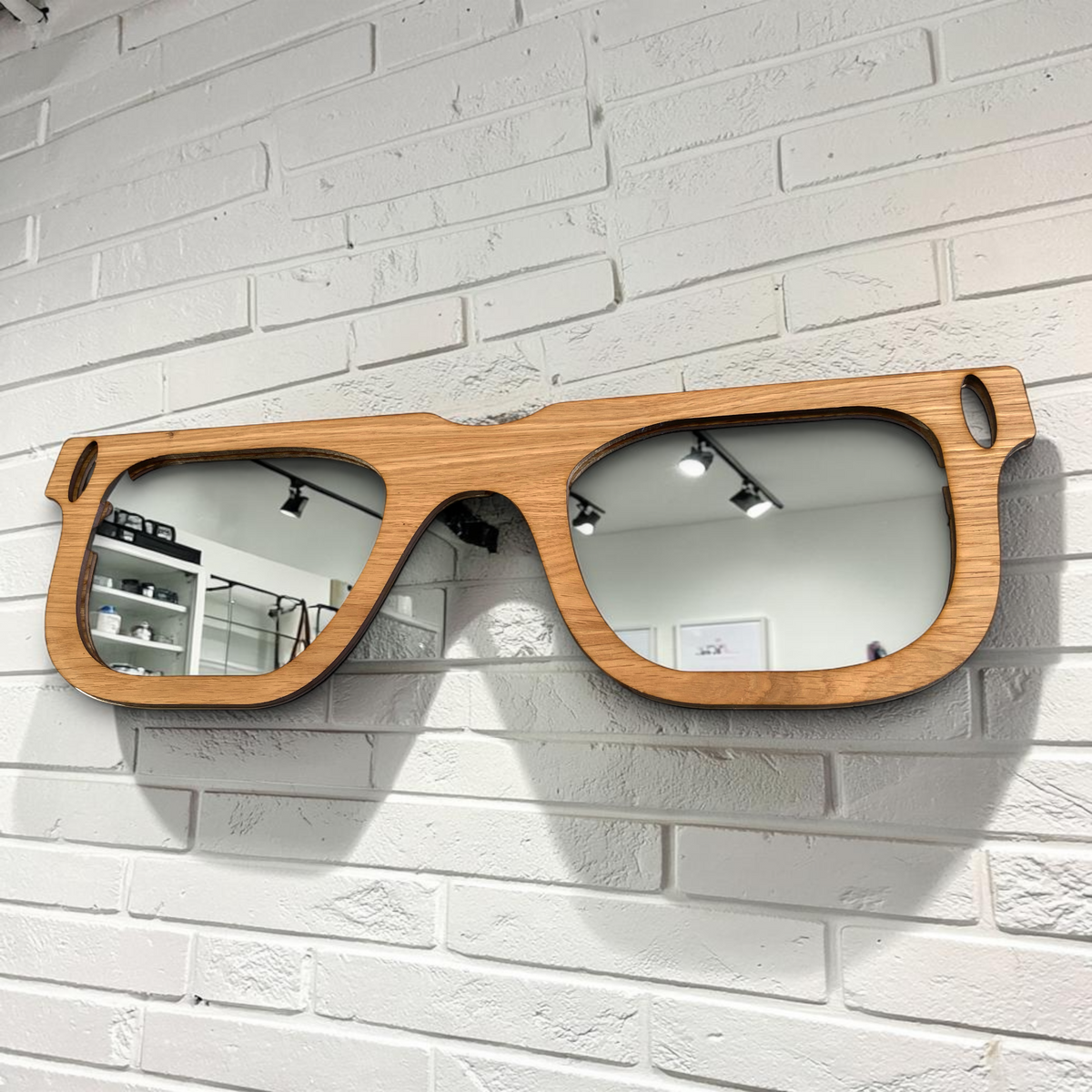 Retro glasses-shaped wall mirror with a light wood frame, mounted on a white brick wall.