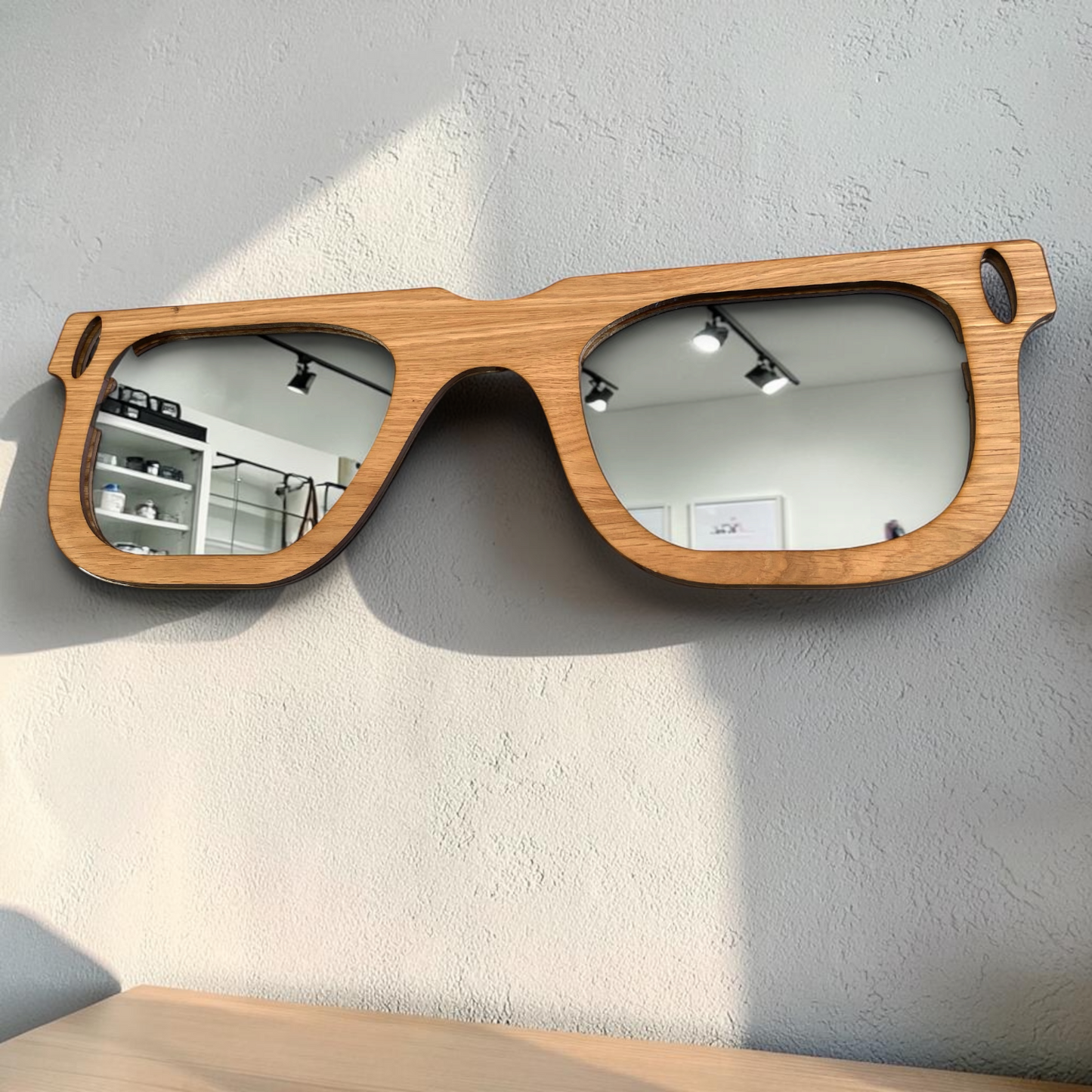 Retro-style wall mirror shaped like a pair of eyeglasses, made from natural wood with two reflective lenses.