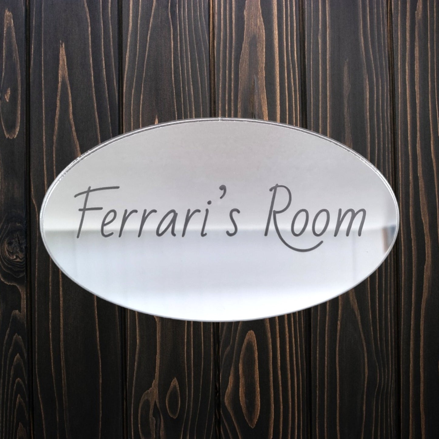 Oval mirrored door sign engraved with "Ferrari's Room" in script, mounted on dark wood.