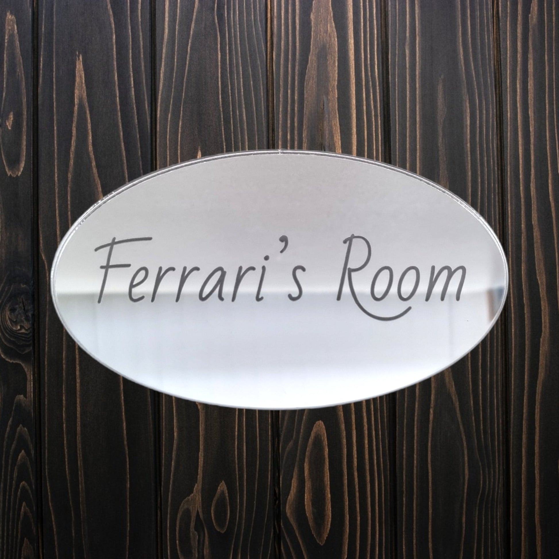 Oval mirrored door sign engraved with "Ferrari's Room" in script, mounted on dark wood.