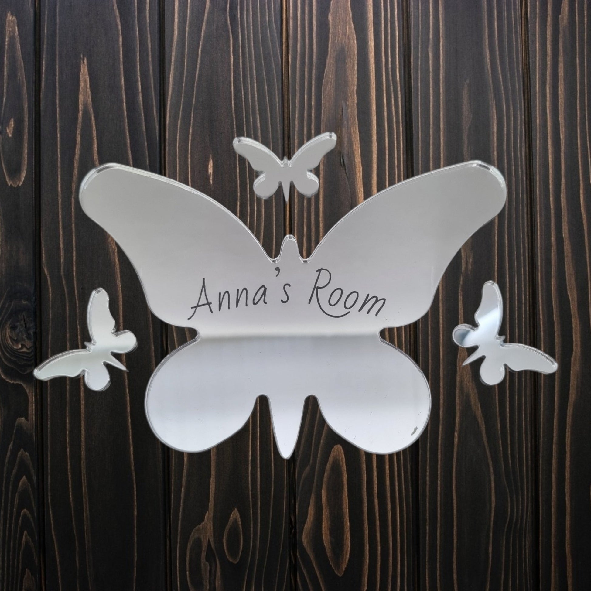 Personalised butterfly mirrored door sign with "Anna's Room" engraved on a dark wooden background.