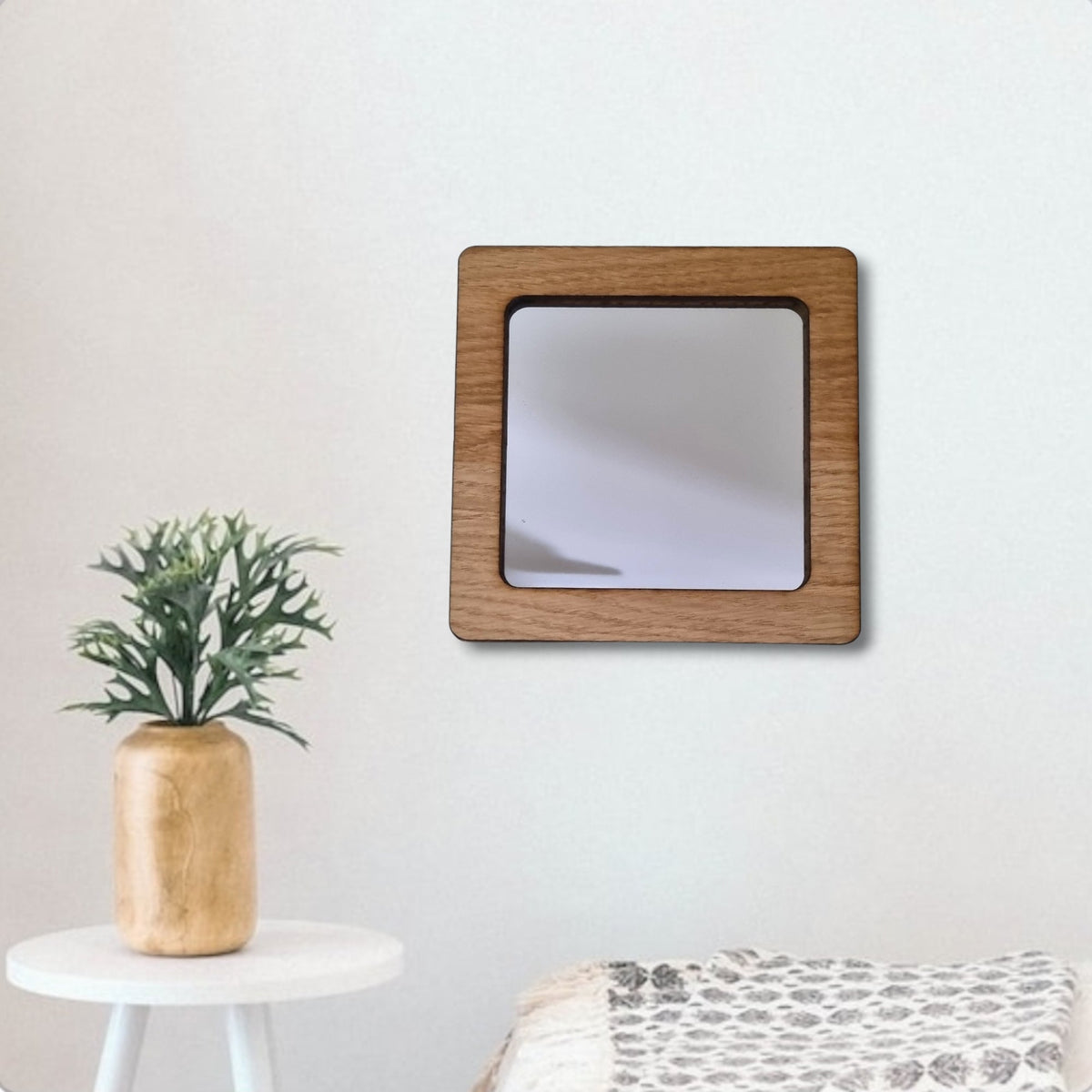 A square wall mirror with a thick brown wooden frame hangs against a plain white wall.