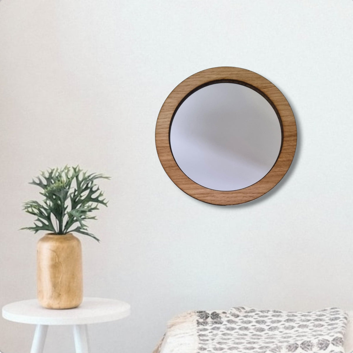 Round mirror with a light brown wood frame hanging on a plain white wall.