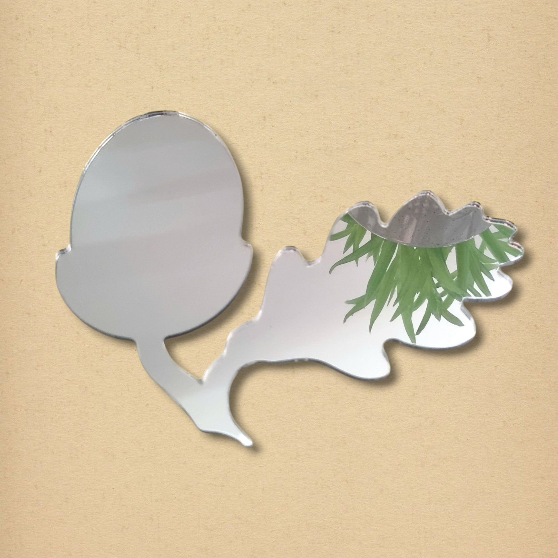 An acorn and oak leaf shaped silver mirror on a light brown background.