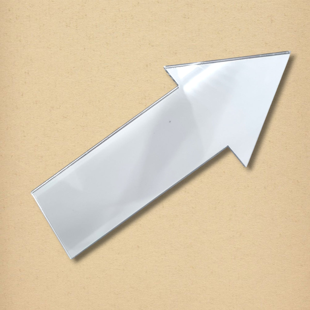 An arrow-shaped acrylic mirror against a light brown textured background.