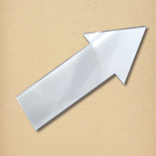 An arrow-shaped acrylic mirror against a light brown textured background.