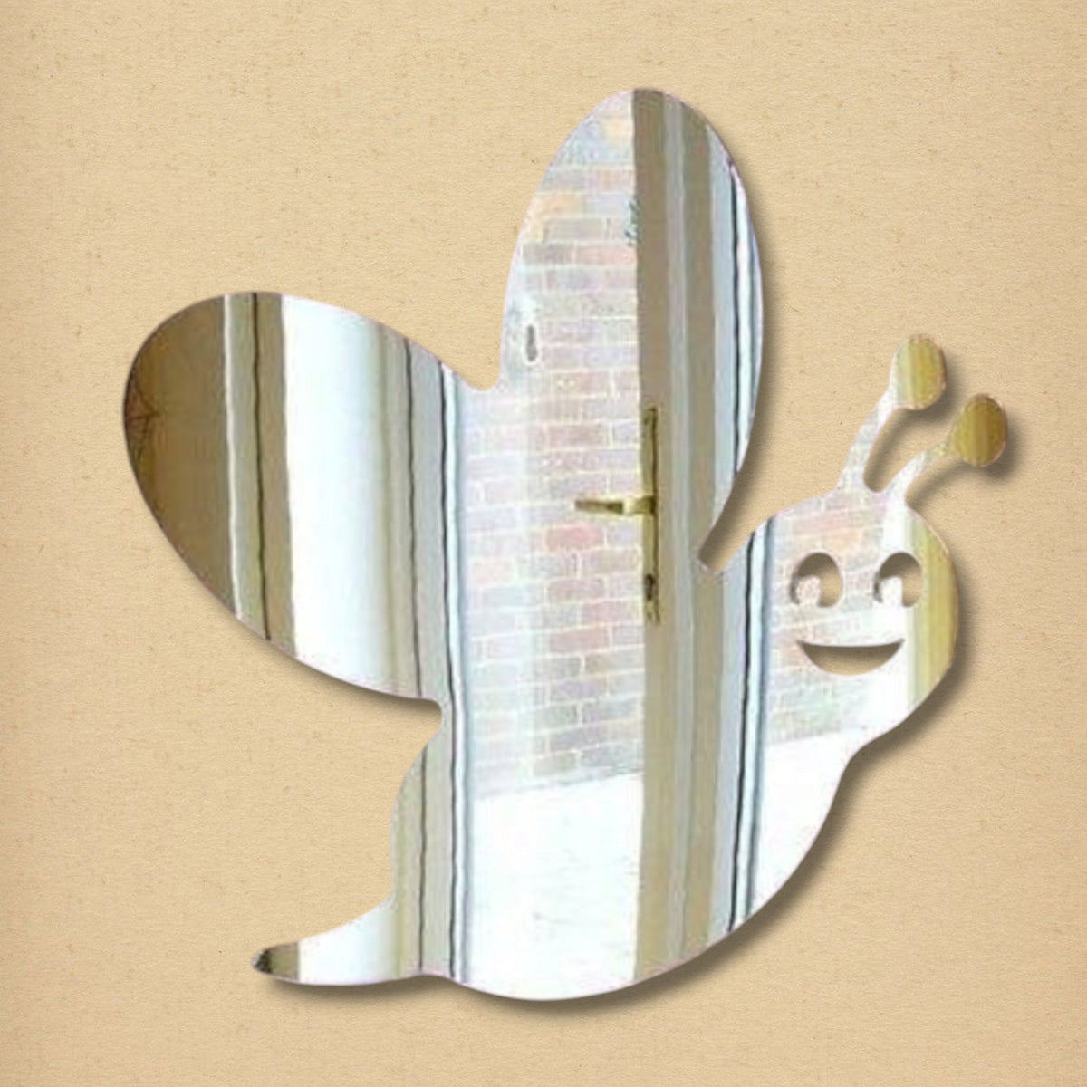 Bee-shaped mirror with cutout eyes, a smiling mouth, antennae, and wings, reflecting a room.