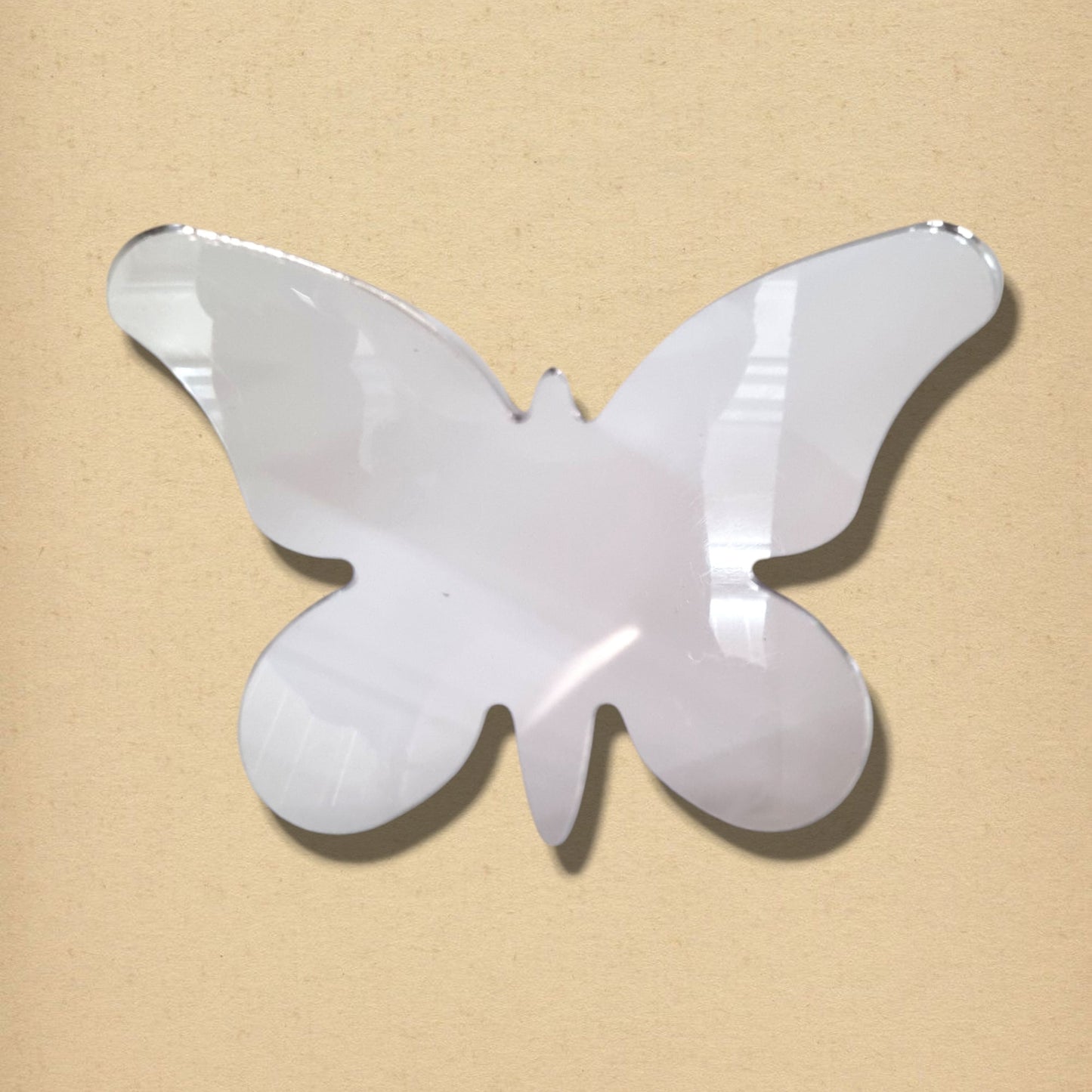 Butterfly-shaped silver mirror with long wings on a beige background.