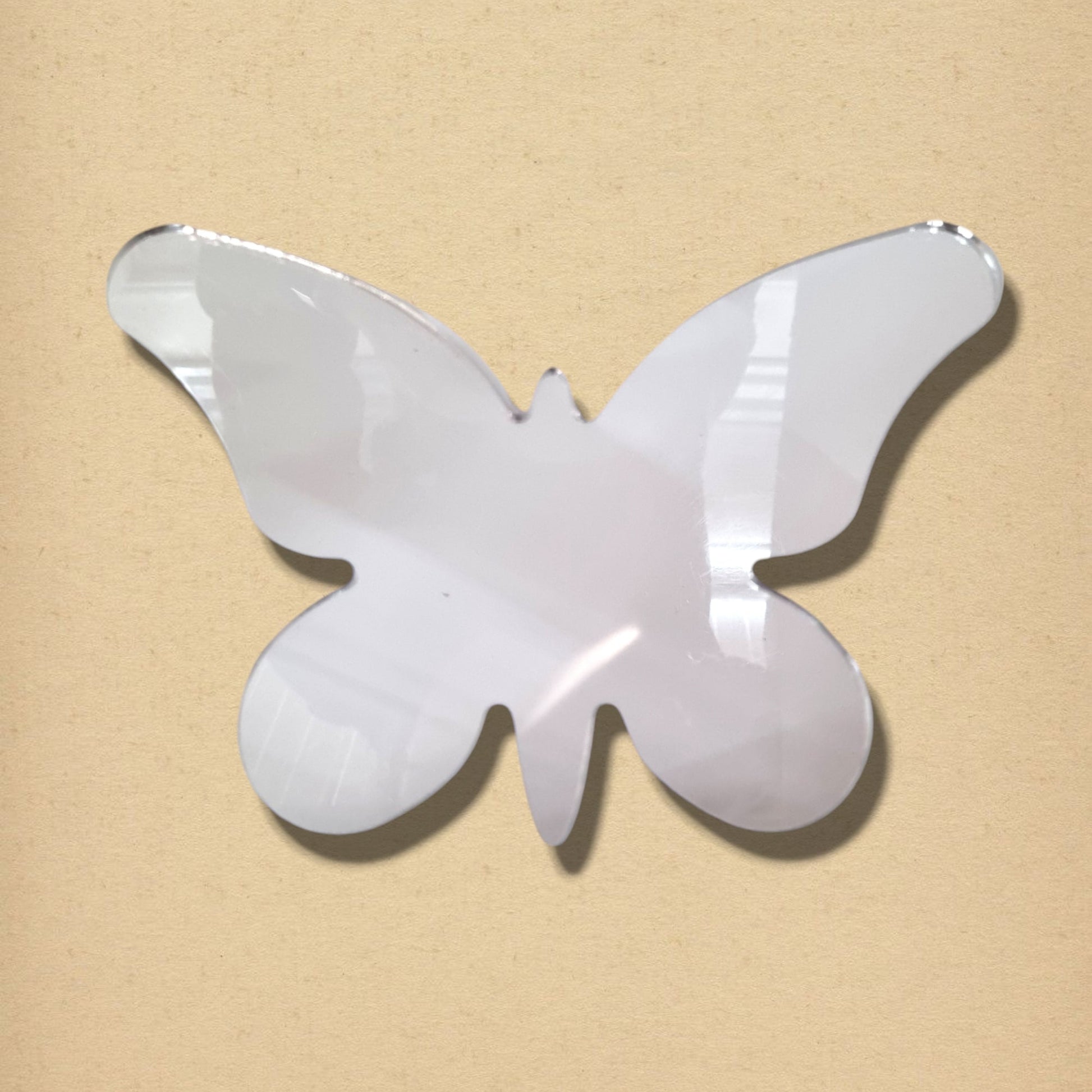 Butterfly-shaped silver mirror with long wings on a beige background.