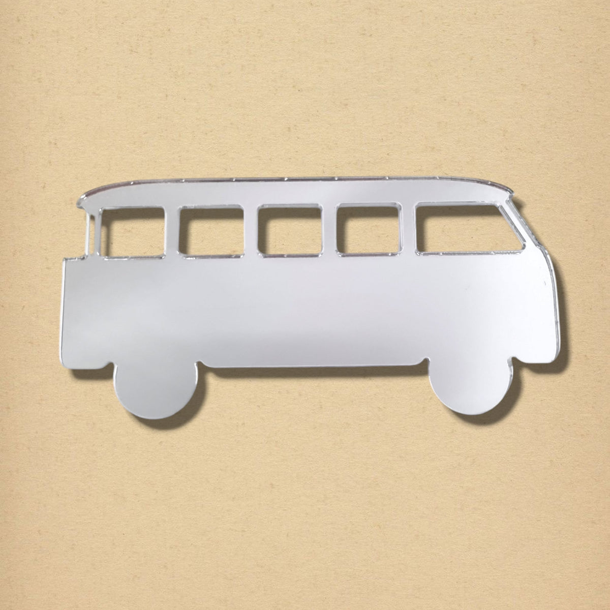 Silver camper van-shaped mirror with cutout windows against a light brown background.