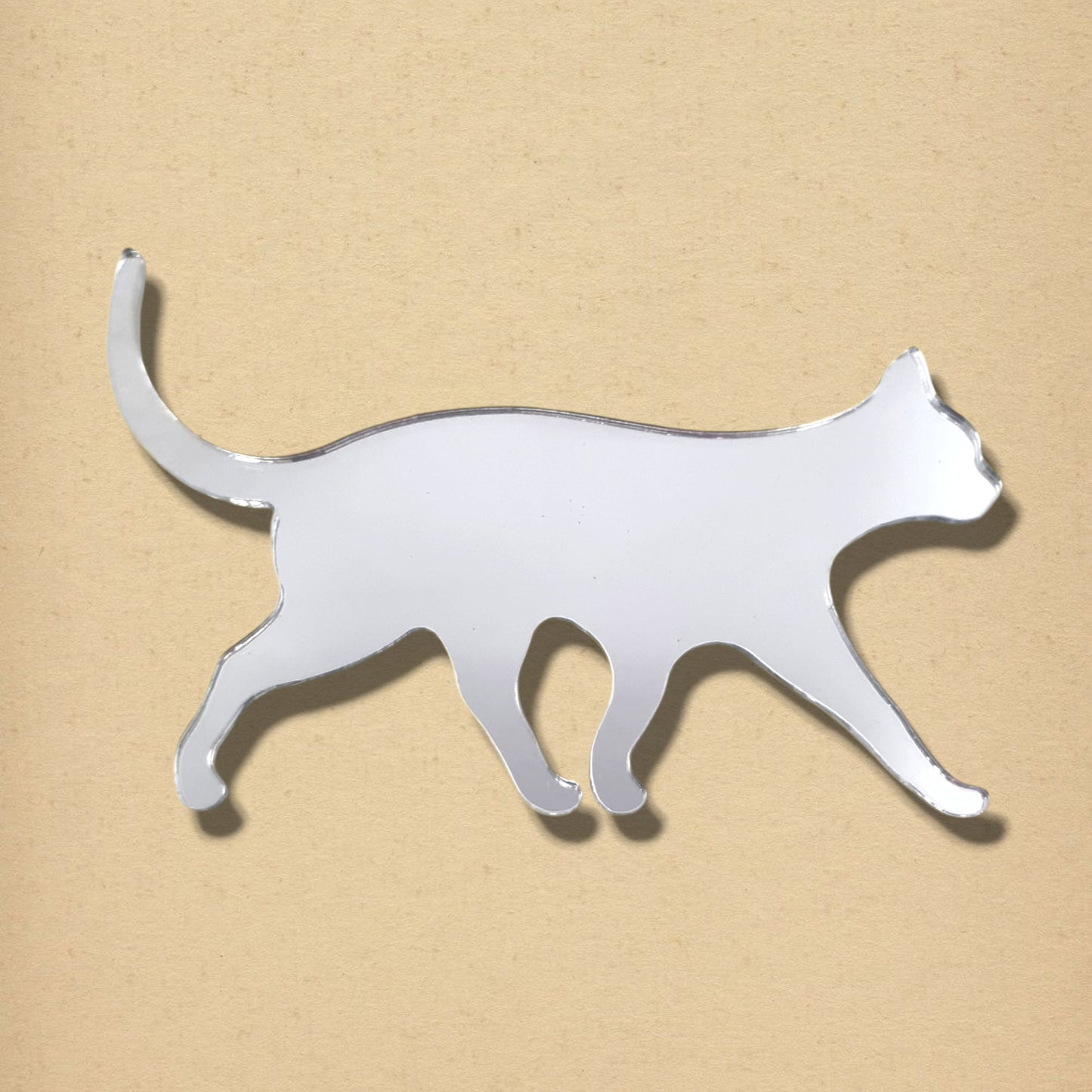Walking cat-shaped acrylic mirror in silver on a tan background.