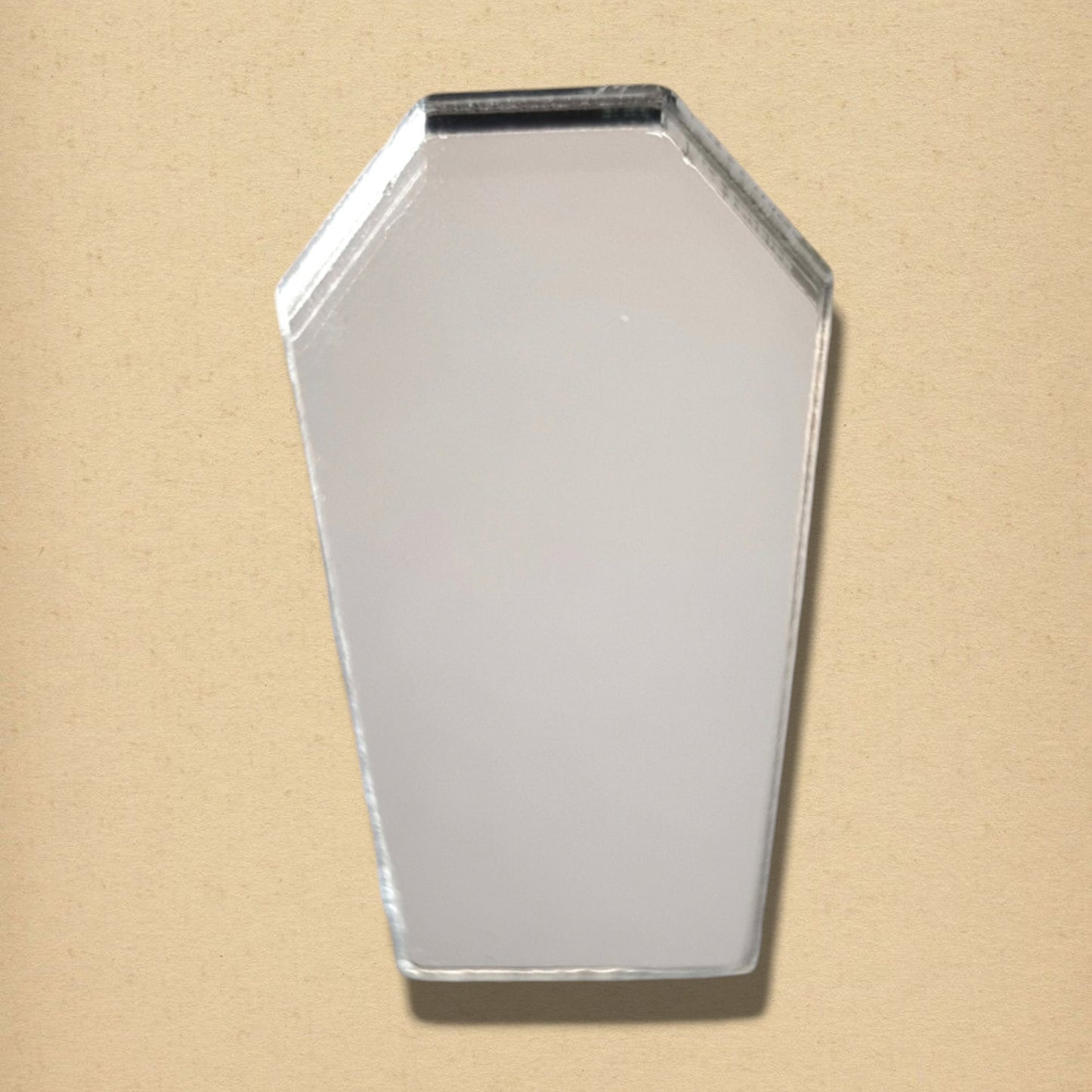 A coffin-shaped glass mirror with beveled edges against a plain tan background.