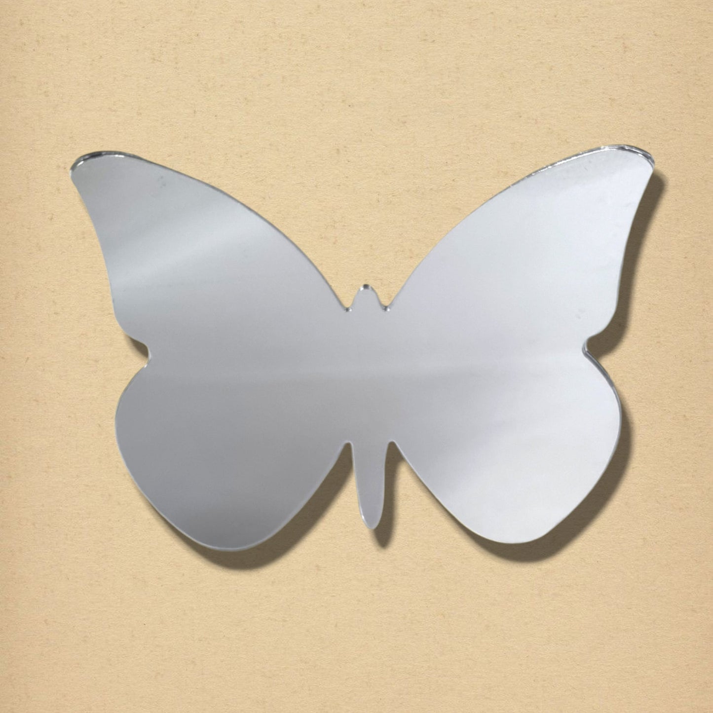 Silver butterfly-shaped mirror with big wings on a textured beige background.