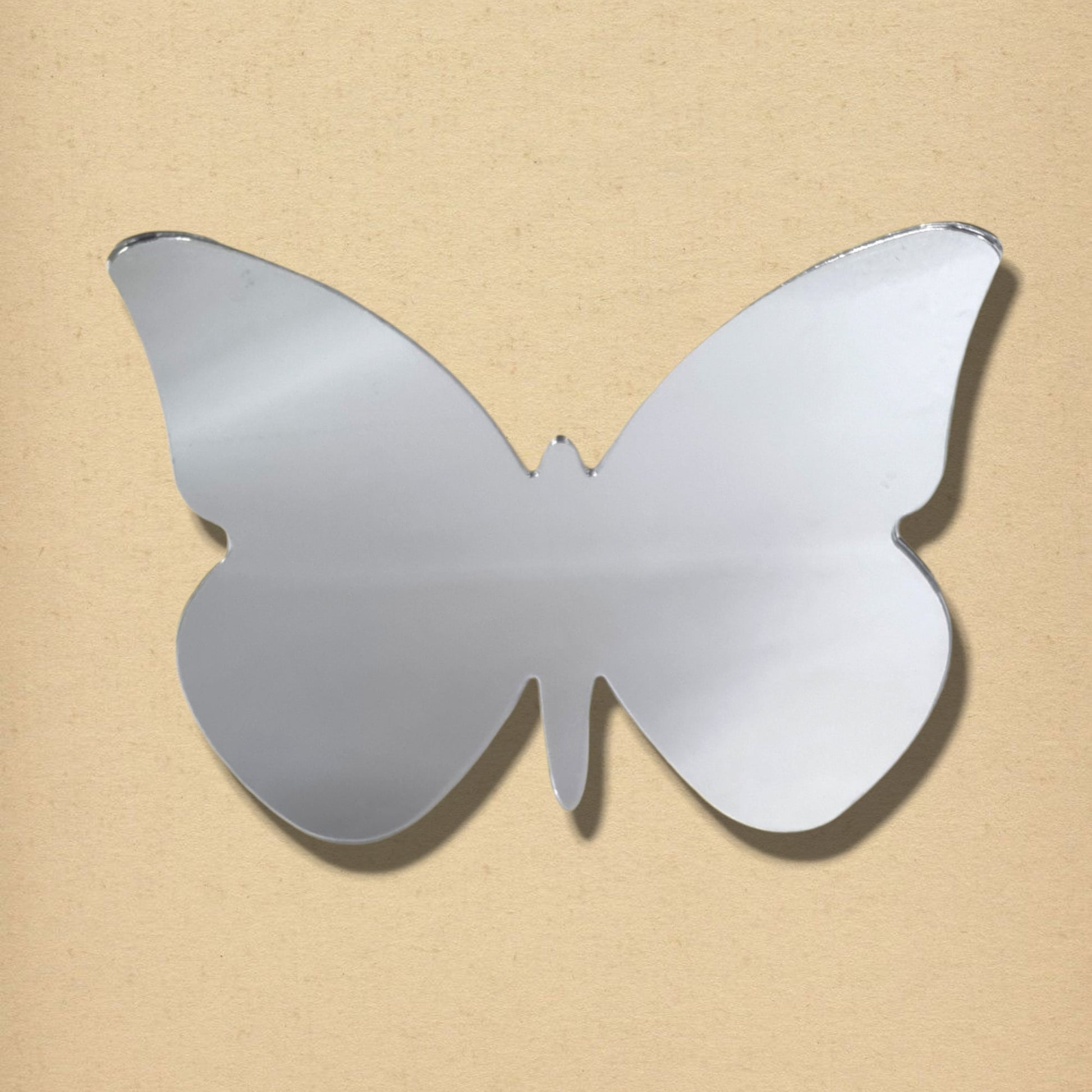 Silver butterfly-shaped mirror with big wings on a textured beige background.