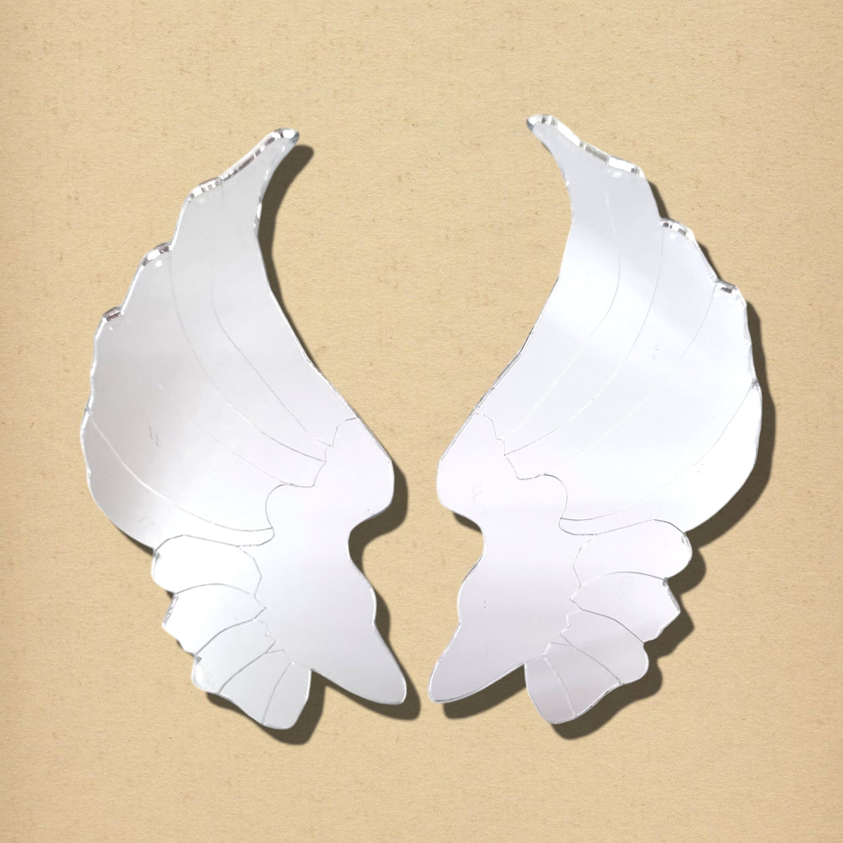 Two reflective, feather-shaped mirror pieces form a pair of angel wings on a tan background.