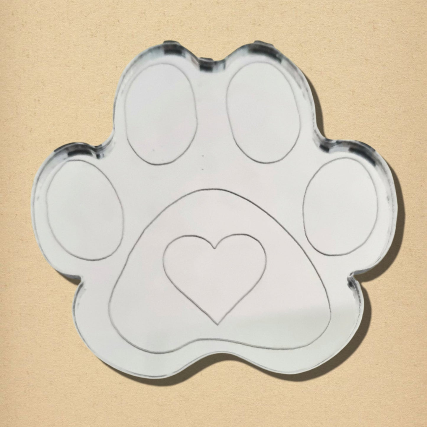Dog paw print-shaped mirror with engraved toe beans and a central heart outline.