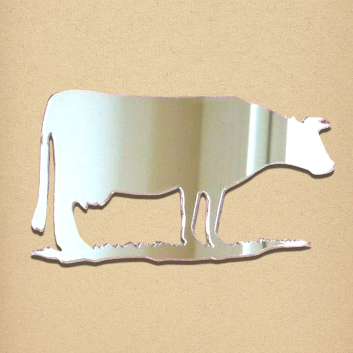 A reflective cow-shaped mirror on a textured tan background.