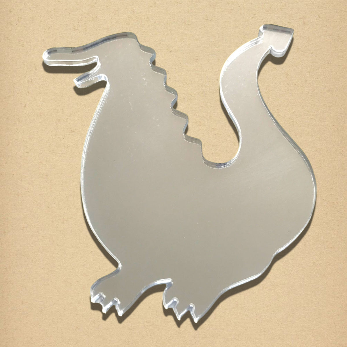 A reflective dragon-shaped acrylic mirror on a tan surface.