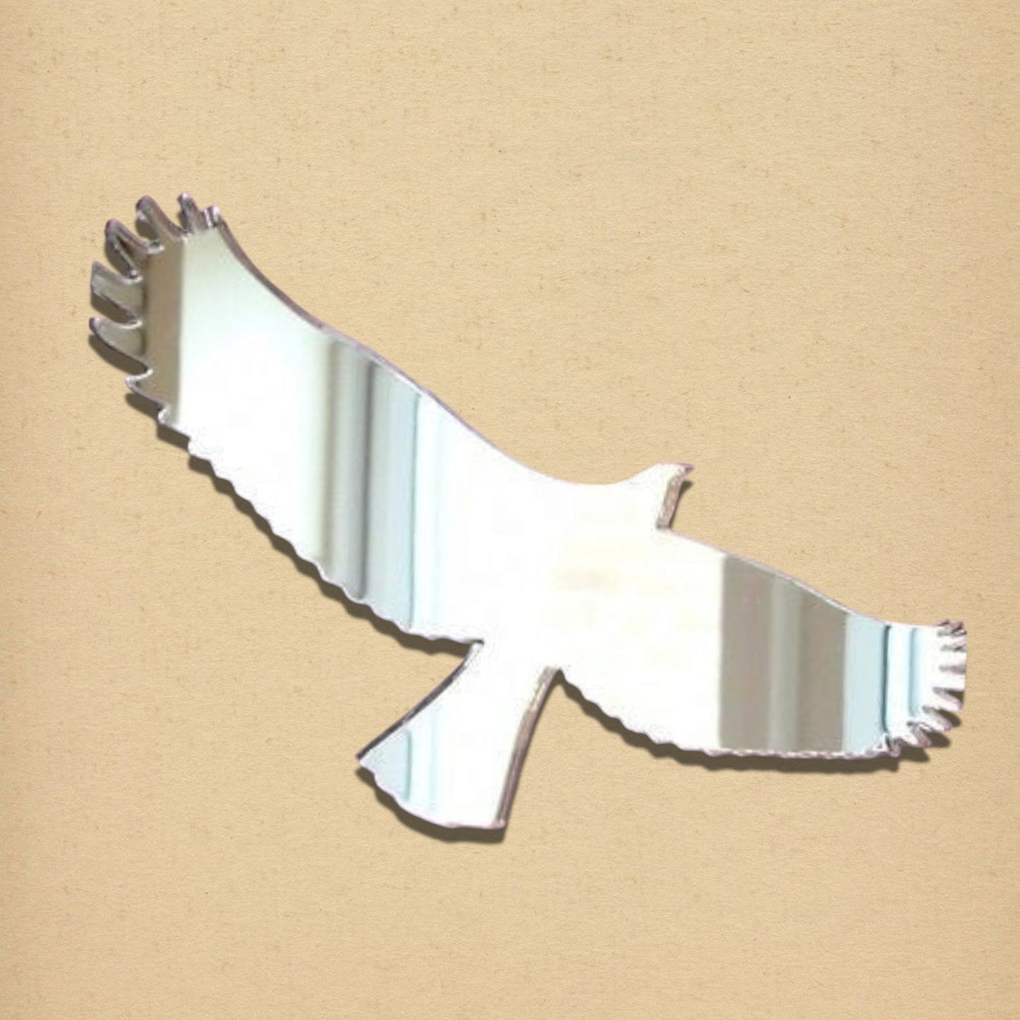 Eagle-shaped acrylic mirror in silver, displayed on a textured beige surface.