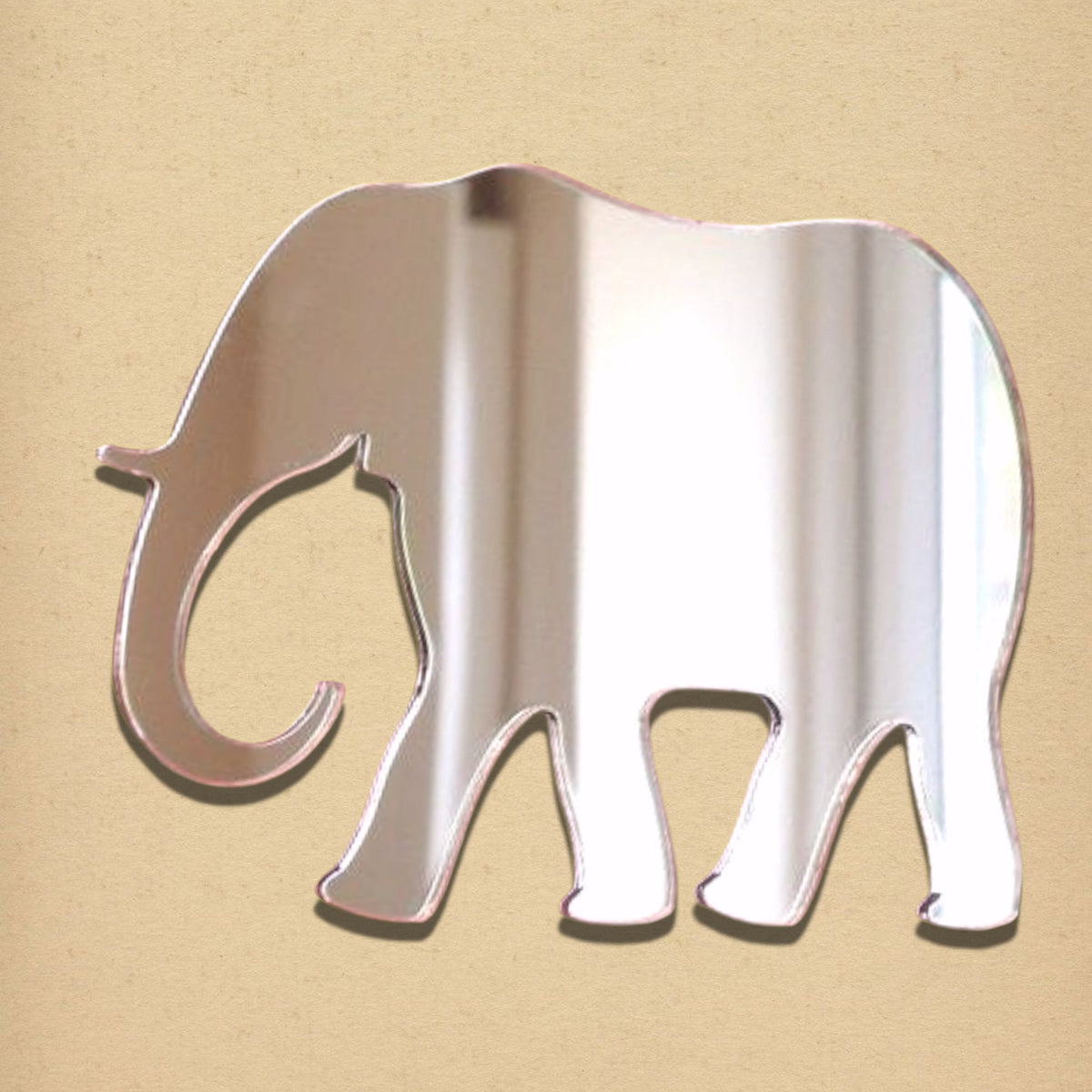 An elephant-shaped mirror with a reflective surface and pink edges on a tan background.