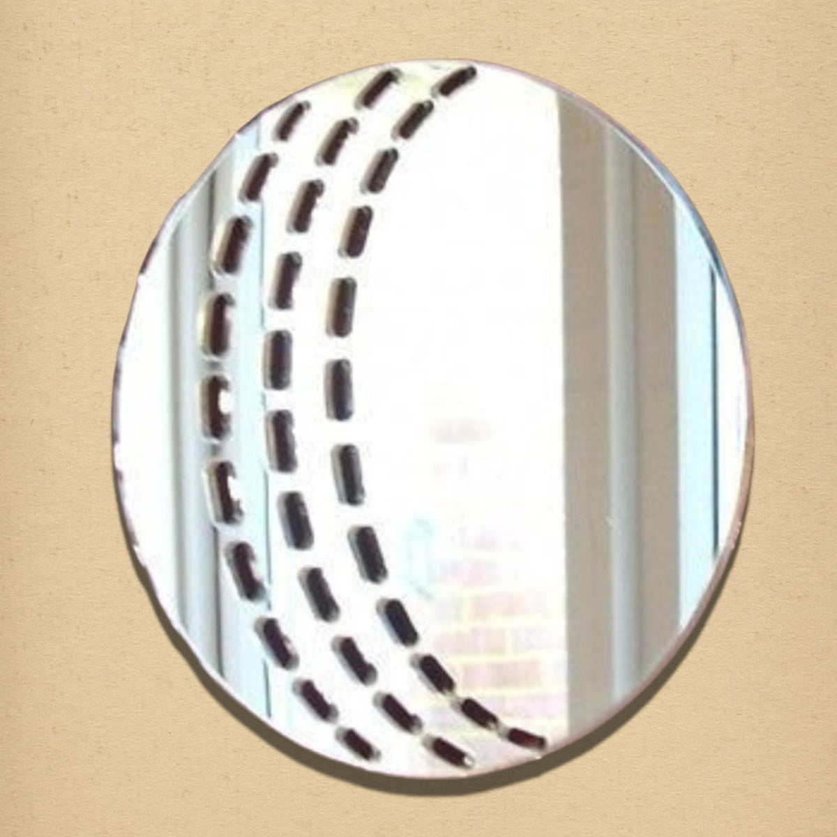 A circular mirror shaped like a cricket ball, featuring etched curved seams of dashed lines.