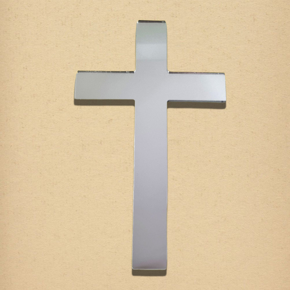 Cross-shaped silver acrylic mirror on a tan textured background.