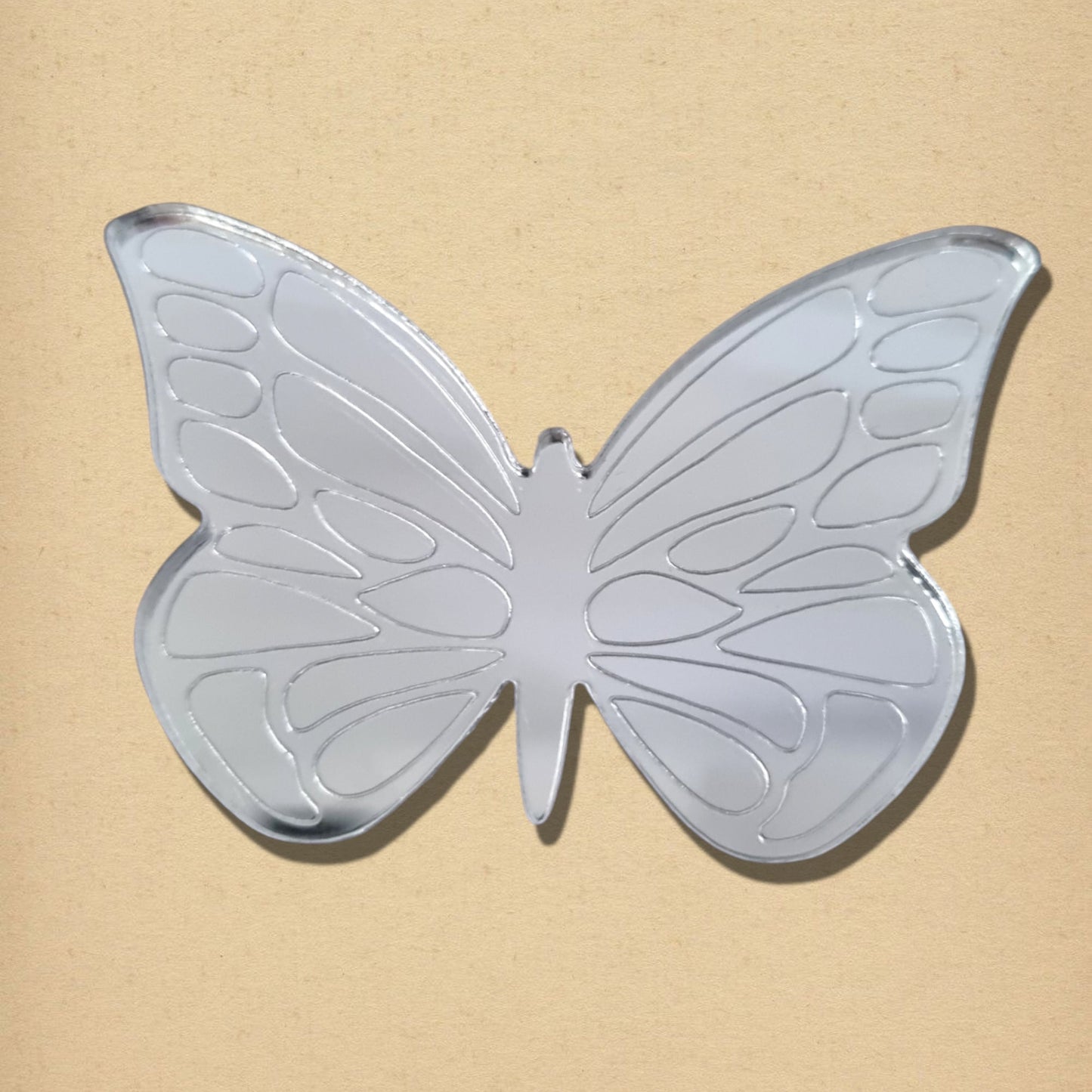 Silver butterfly-shaped mirror with etched wing details against a textured neutral background.