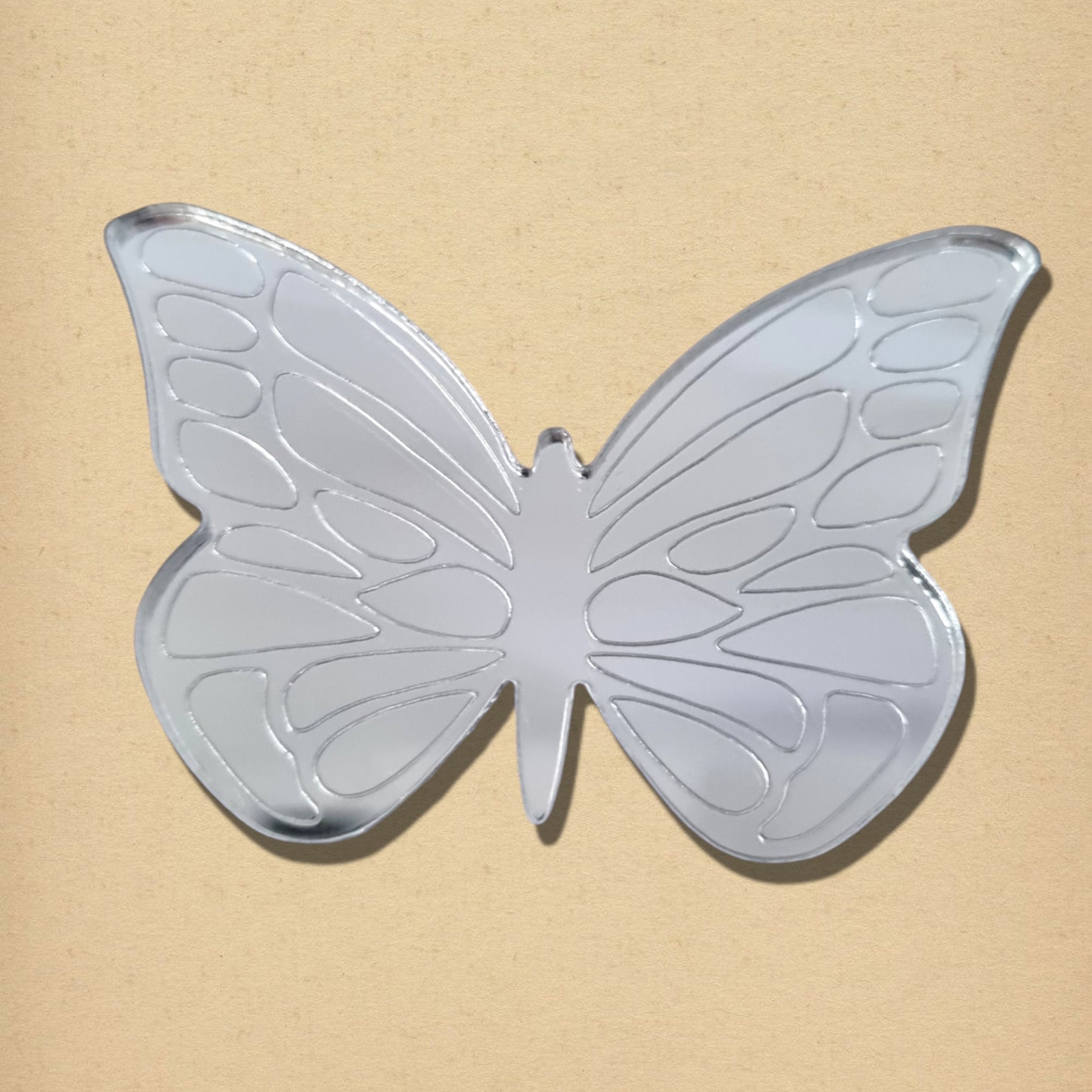 Silver butterfly-shaped mirror with etched wing details against a textured neutral background.
