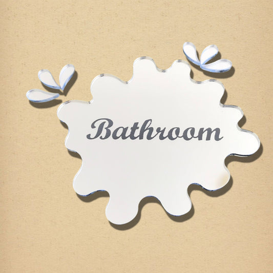 Mirrored puddle-shaped bathroom sign with engraved text and two separate droplet pieces on beige background.