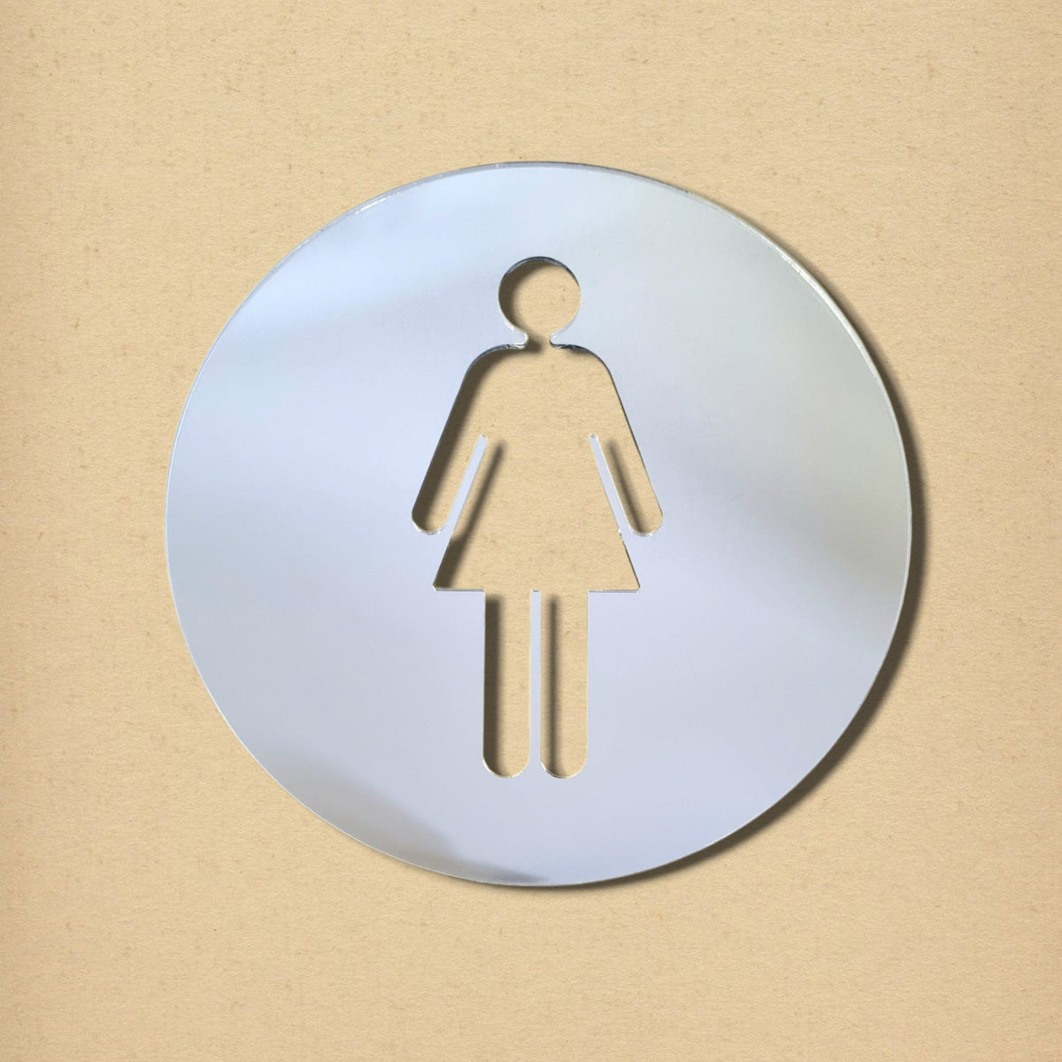 Round mirrored female toilet sign with a cutout woman symbol on a beige background.