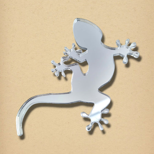 Gecko-shaped mirror with a reflective surface, shown on a neutral textured background.