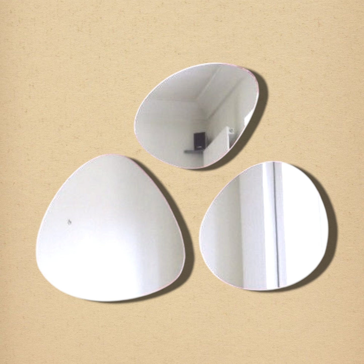 Three organic, pebble-shaped wall mirrors arranged on a textured beige background.