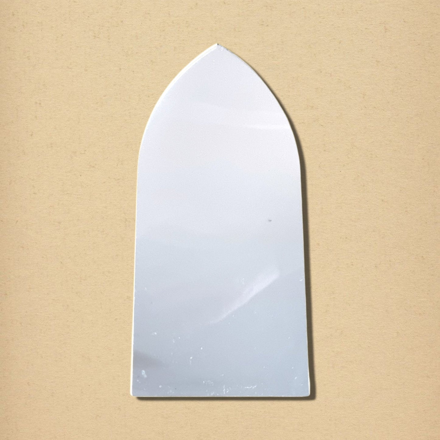 Gothic arch mirror with a pointed top and flat bottom, centered against a tan background.
