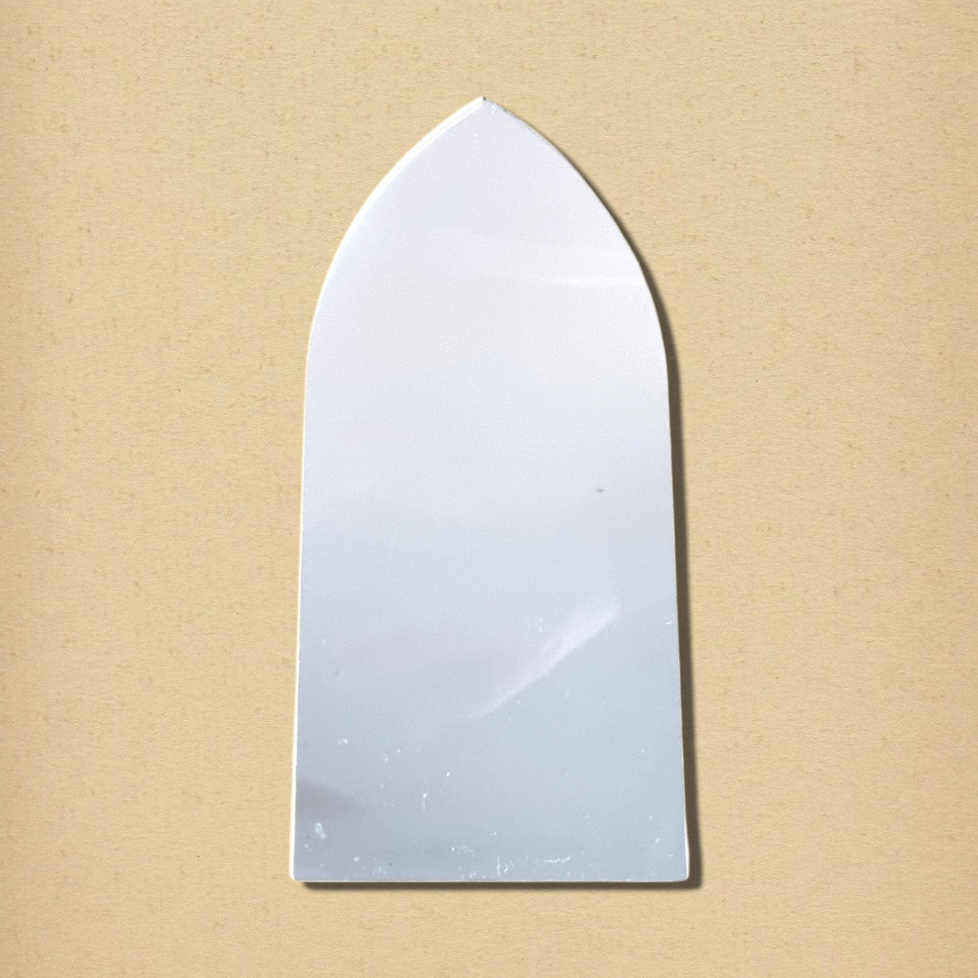 Gothic arch mirror with a pointed top and flat bottom, centered against a tan background.