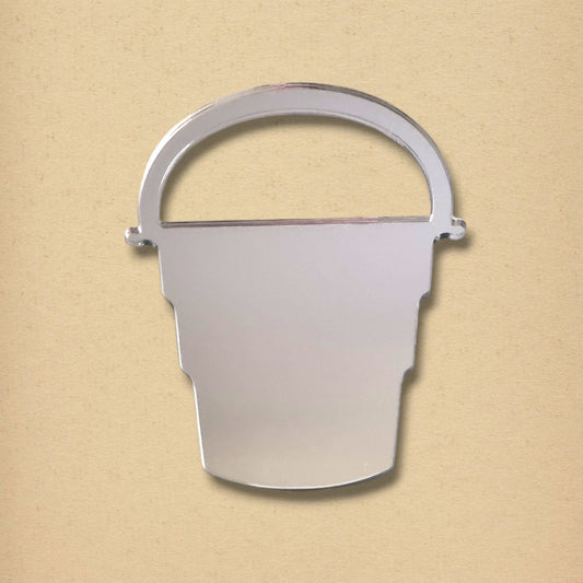 Silver bucket-shaped wall mirror with an arched handle on a beige background.