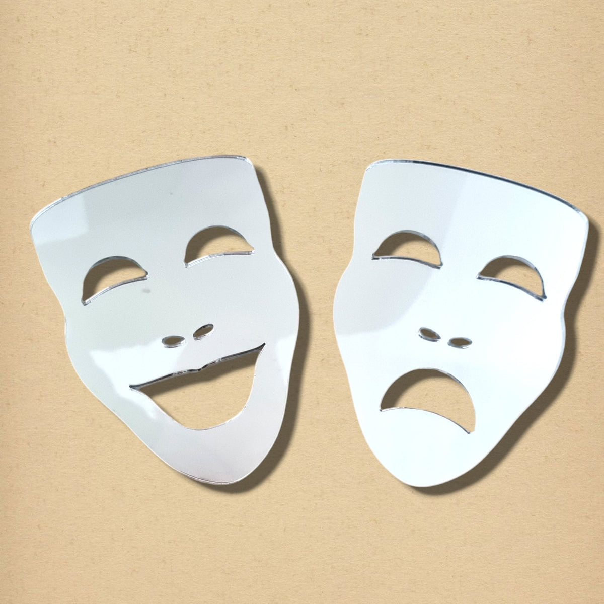 Two mirror theatre masks, one smiling comedy mask and one frowning tragedy mask, on a neutral beige background.