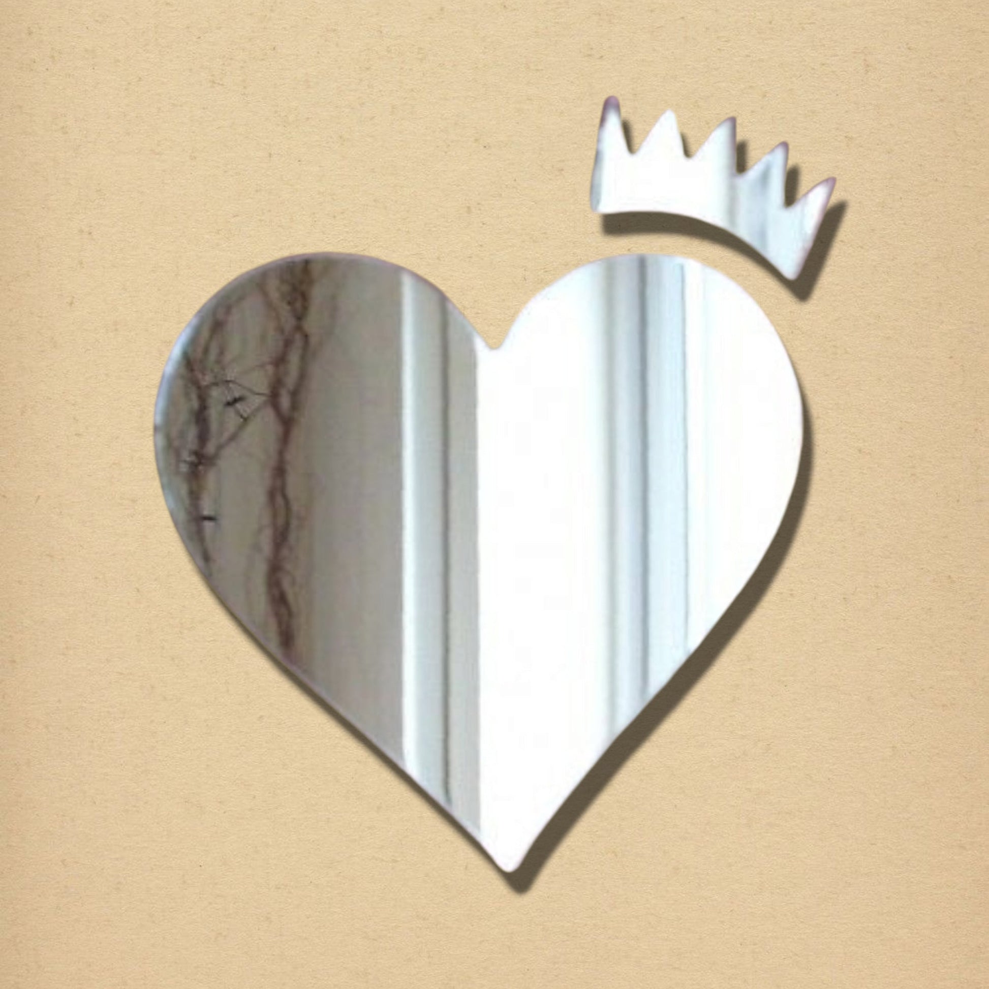Heart and crown shaped silver wall mirror on a tan textured background.