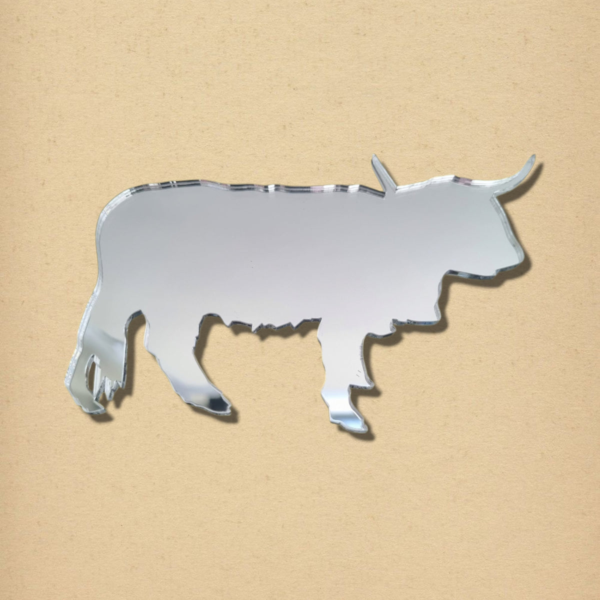 A silver Highland cow-shaped mirror with horns on a tan background.