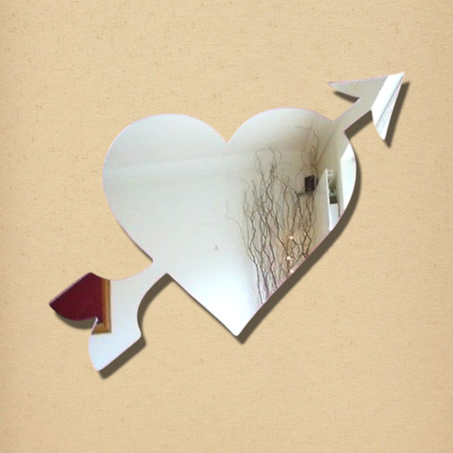 A heart-shaped mirror with an arrow running diagonally through it, on a beige background.