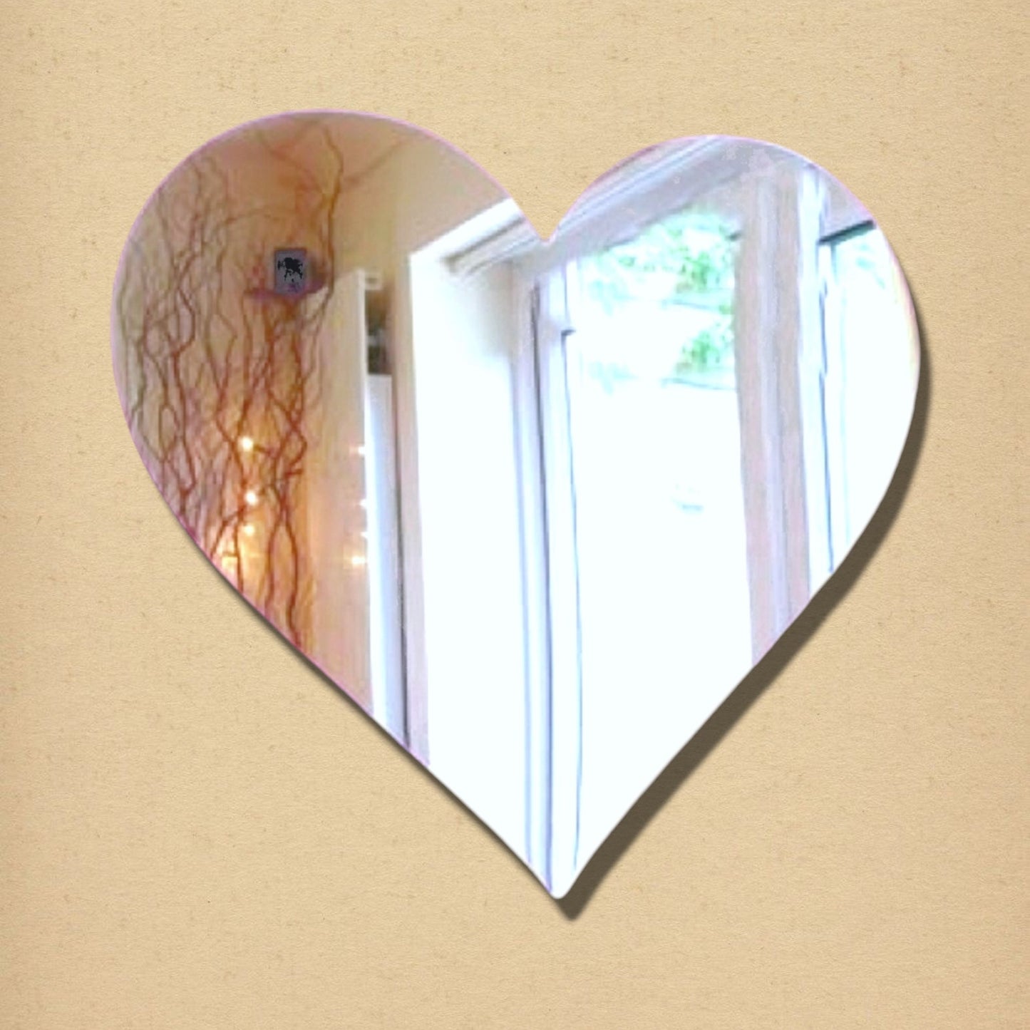 A heart-shaped wall mirror reflecting a room interior, mounted on a tan background.